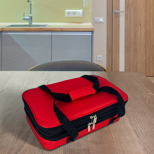 The Le Regalo 5 Piece Bake & Take Set, a red soft-sided insulated carrier with black handles, is placed on a wooden table in a modern kitchen featuring a sink and light wood cabinets.