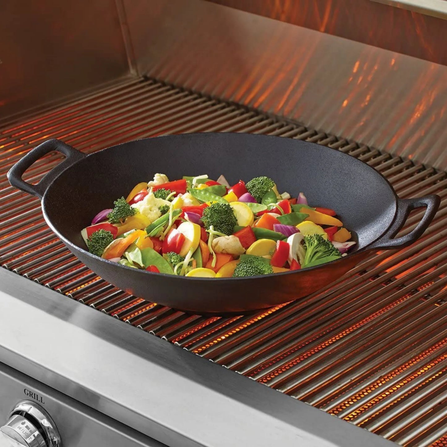 The Jim Beam 12 Cast Iron Wok, pre-seasoned and loaded with vibrant broccoli, bell peppers, and onions, rests atop stainless steel grill grates—showcasing this essential Jim Beam cookware in action.