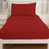 A neatly made bed features the Textilia Bedsheet Set by Textilia in burgundy brushed microfiber—includes bedsheets, pillowcase, and comforter—on a white frame in a bright room with sheer curtains and a small bedside table.