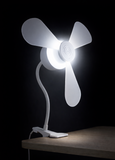 The North Point Clip Light with Fan 11W, featuring a flexible gooseneck and three blades, is securely clipped to a wooden table edge and glows brightly against a dark background.