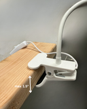 The North Point Clip Light with Fan 11W features a flexible gooseneck and attaches easily to surfaces up to 1.5 inches thick. Its white clamp design includes a visible power cord, ideal for desks or workspaces.