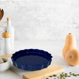 The Le Regalo Stoneware Pie Dish in dark blue rests on a wooden cutting board beside butternut squash, white salt and pepper shakers, a mortar and pestle, and pumpkin seeds—ideal for baking homemade pies.