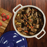 A Le Regalo Stoneware Casserole with Lid, filled with beef stew—tender meat, carrots, and potatoes—rests on a wooden table. A blue lid sits beside it, alongside a cutting board topped with vine tomatoes for a hearty meal.