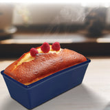 A freshly baked loaf cake in a blue Le Regalo Stoneware Loaf Pan, topped with three raspberries and visible steam, rests on a light surface with a softly blurred background—highlighting Le Regalo’s baking versatility and quality.