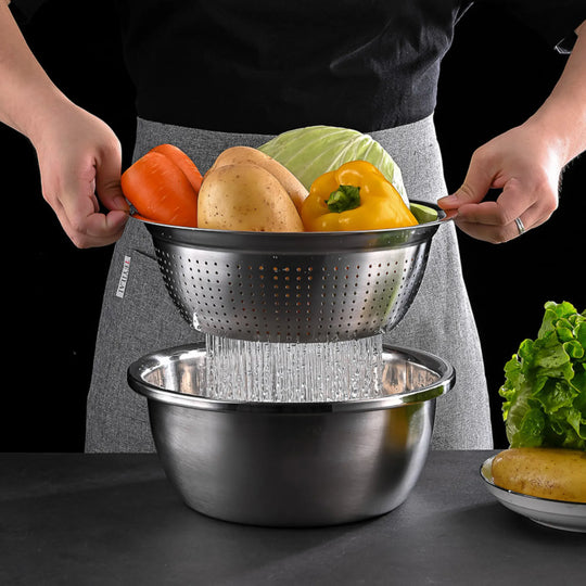Someone holds a Le Regalo 5 Piece Stainless Steel Colander filled with bell pepper, potato, and cabbage over a metal bowl as water drains, while lettuce rests nearby—showcasing Le Regalo’s versatile kitchenware for daily meal prep.