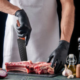 Wearing a white apron and black gloves, a person uses a stainless steel knife to cut raw meat on a black cutting board, with garlic, red onion, oil, a pepper grinder, and the Le Regalo 5 Piece Kitchen Knife Set with Magnetic Holder nearby.