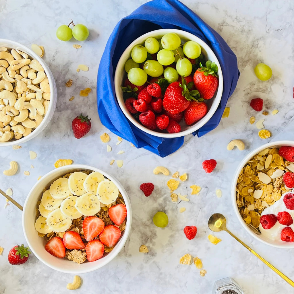 The Le Regalo 4 Piece Stoneware Bowl Set, shown on marble, holds cashews, grapes with strawberries, cereal with fruit, and granola. Scattered fruit and spoons highlight these stylish oven-safe bowls by Le Regalo.