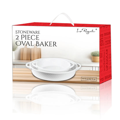 The Le Regalo 2 Piece Stoneware Oval Baker Set features two white stoneware baking dishes with handles, shown on a kitchen countertop beside wooden utensils and a potted plant.