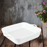 The Le Regalo 10 Stoneware Square Baker by Le Regalo, an oven-safe ceramic dish with handles, sits on a rustic wooden table next to a woven basket of purple and pink flowers, against a textured gray wall.