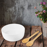The Le Regalo 3 Piece Salad Server Set sits on a rustic wooden table beside a white textured stoneware bowl, with wildflowers in a wicker basket and a gray textured wall providing an inviting backdrop for elegant dining.