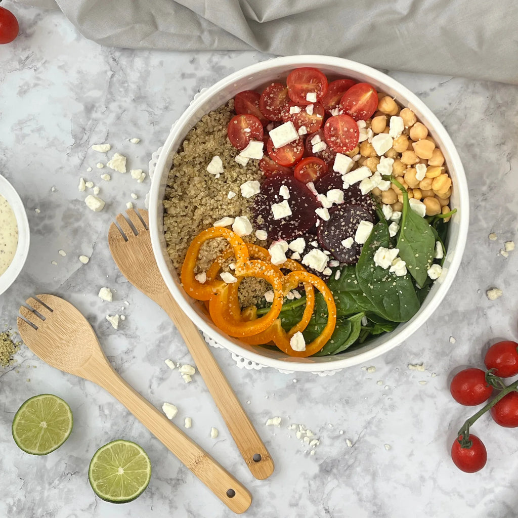 A bowl of salad with quinoa, spinach, cherry tomatoes, chickpeas, yellow bell pepper, feta cheese, and beets is served in a Stoneware Salad Bowl. The Le Regalo 3 Piece Salad Server Set by Le Regalo completes this elegant tableware setting on marble.