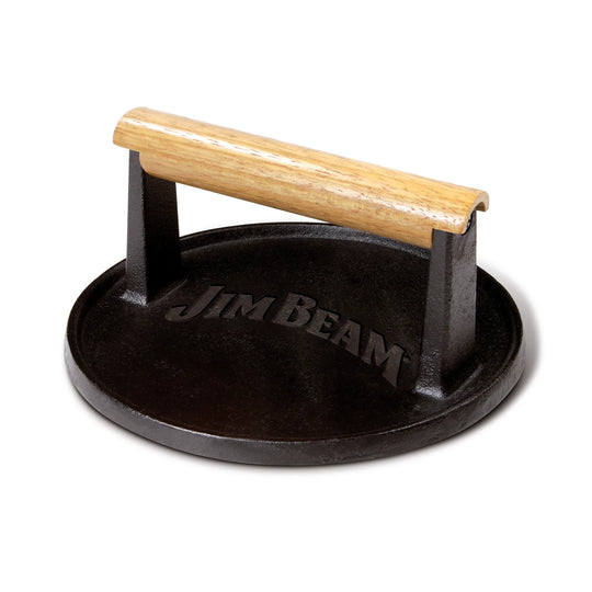 Five burger patties cook on a grill, with the Jim Beam Cast Iron Burger Press—featuring a wooden handle—on one patty. Flames and hot coals glow below, creating an ideal scene for any grilling enthusiast or cast iron cookware fan.