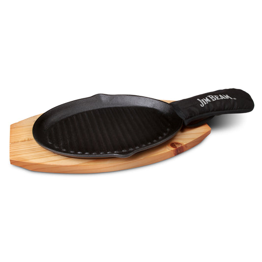 Jim Beam® black cast iron skillet set with "Jim Beam" printed on the mitten which is covering the handle, resting on a wooden trivet, isolated on a white background.