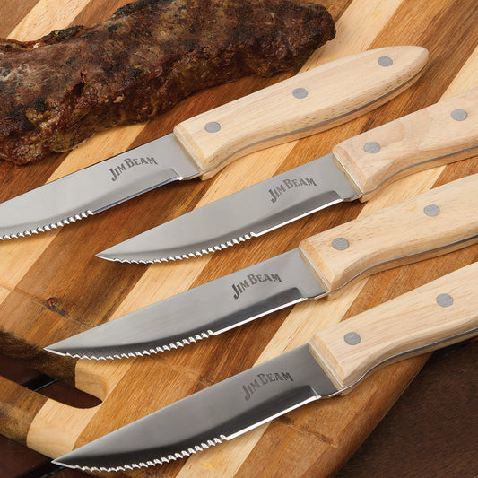 The Jim Beam 4 Piece Serrated Steak Knife Set is neatly arranged on a wooden cutting board beside a cooked steak, each knife featuring an ergonomic handle and the Jim Beam logo.