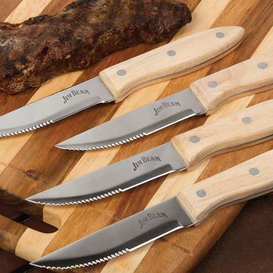 The Jim Beam 4 Piece Serrated Steak Knife Set features stainless steel blades, ergonomic handles with three metal rivets, and the Jim Beam logo on each blade. The four knives are displayed in a horizontal row.