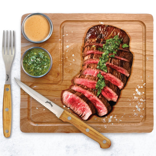 The Jim Beam 2 Pack Steak Serving Set includes parawood boards, a steak knife, fork, coarse salt, and two dipping sauce bowls—everything you need to serve BBQ steak with chimichurri, just like a pro.