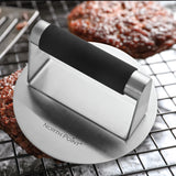 The North Point 3 Piece Burger Kit includes a stainless steel burger press with a black handle, shown on a wire rack beside cooked patties—a perfect kit for burger enthusiasts.
