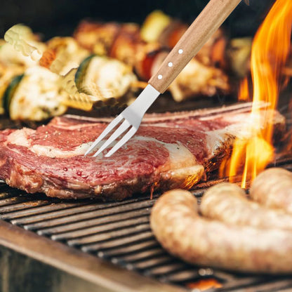 A close-up shows a steak held with a fork from the North Point 5 Piece BBQ Tool Set on the grill, with flames nearby. Sausages and skewers of grilled vegetables also cook over the heat. Brand: North Point.