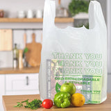 Eco-Friendly Oxo-Biodegradable T-Shirt Carry Bag with  "Thank You" text written is placed on a wooden table with a kitchen background with some product inside the bag and some vegetables on the table