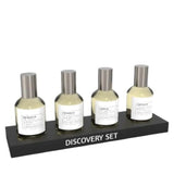 Four Emper Discovery Set bottles from the Luxury Fragrance Collection, each with a silver cap and white label, are arranged on a black DISCOVERY SET stand against a white background—ideal for fragrance enthusiasts.
