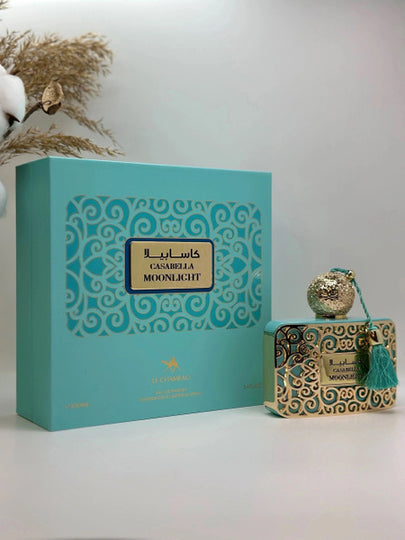 A turquoise and gold Casabella Moonlight Eau de Parfum Spray for Women 3.4 OZ by North Point stands beside an ornate perfume bottle with a tassel and gold accent, set against a neutral backdrop with dried plants for a feminine touch.