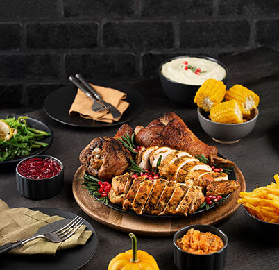 A beautifully arranged plate of roasted meats, corn, mashed potatoes, salad, and sides, set against a dark brick background.